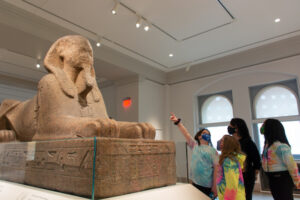 Masked kids examine sphinx at Penn Museum