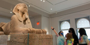 Children at a museum looking at a sphinx statue