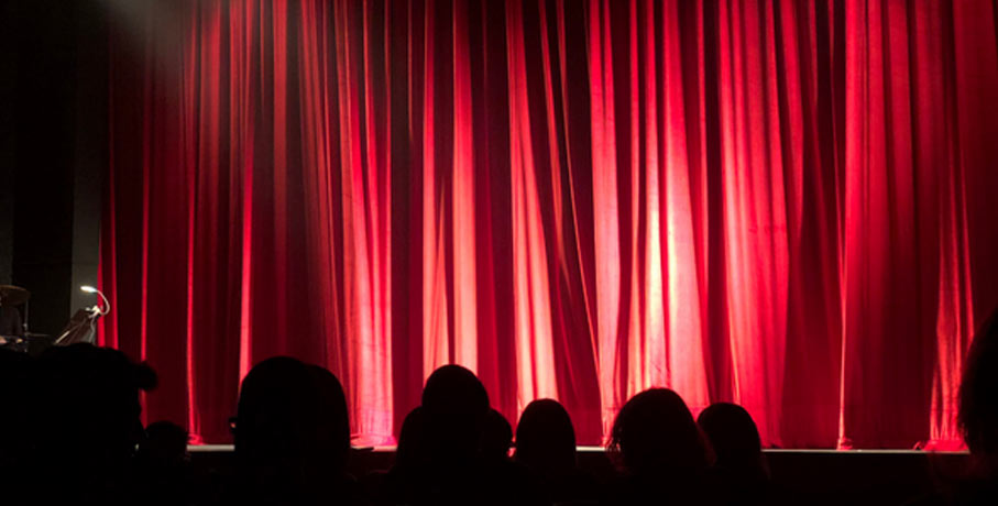 Red theater curtains with silhouette of audience in foreground